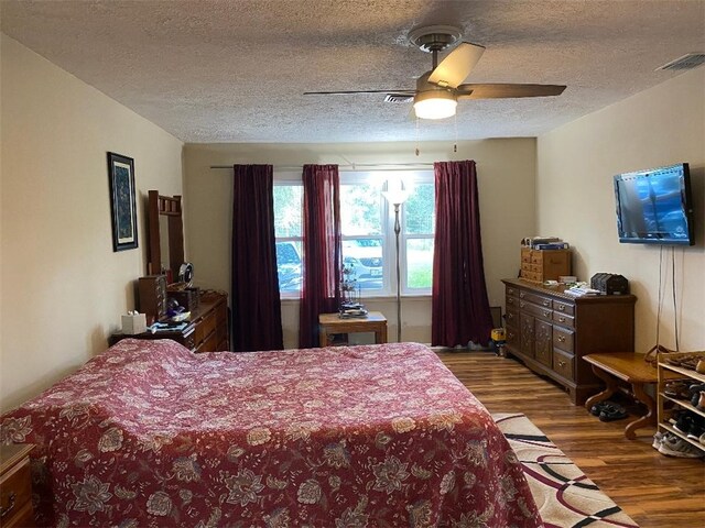 bedroom with a textured ceiling, wood-type flooring, and ceiling fan