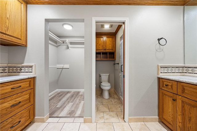 full bathroom featuring vanity, toilet, a walk in closet, tile patterned floors, and backsplash