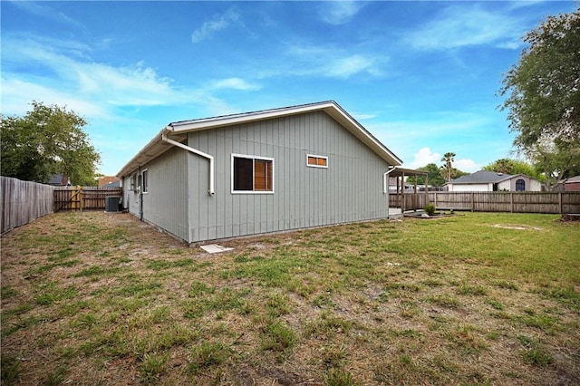 view of side of property with central AC unit, a fenced backyard, and a lawn