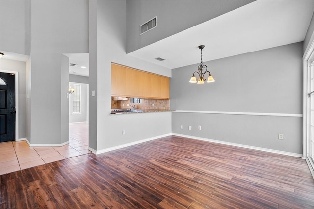 unfurnished living room with baseboards, visible vents, a towering ceiling, wood finished floors, and a chandelier