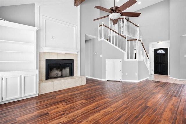 unfurnished living room with stairs, high vaulted ceiling, a tiled fireplace, and wood finished floors