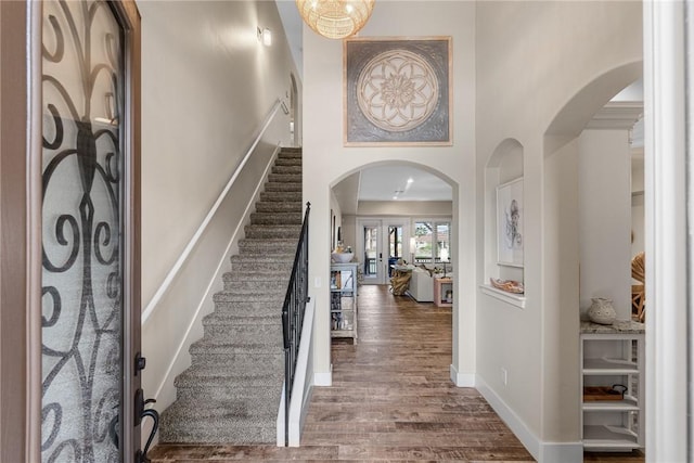 entryway featuring arched walkways, wood finished floors, a towering ceiling, baseboards, and stairs