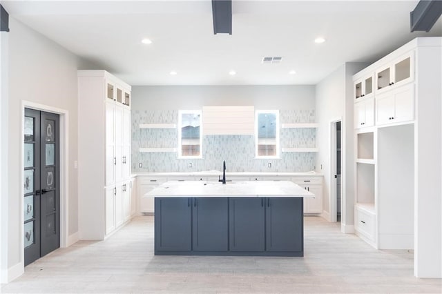 kitchen featuring backsplash, a center island with sink, white cabinetry, and light hardwood / wood-style flooring