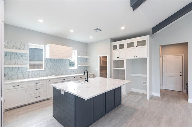 kitchen featuring white cabinetry, light stone countertops, sink, an island with sink, and decorative backsplash