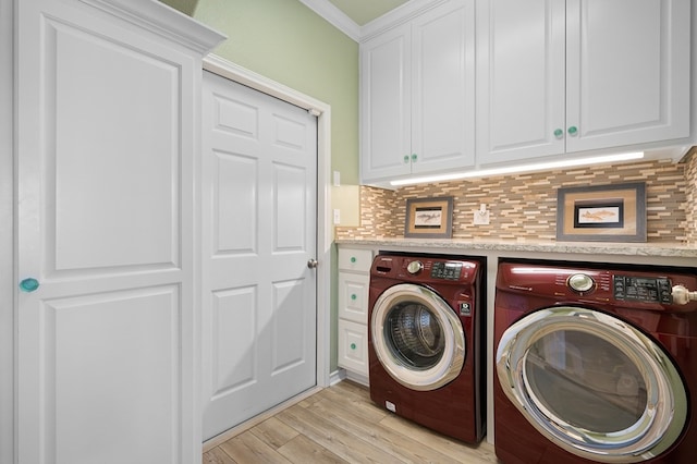 clothes washing area featuring crown molding, light hardwood / wood-style flooring, washing machine and dryer, and cabinets