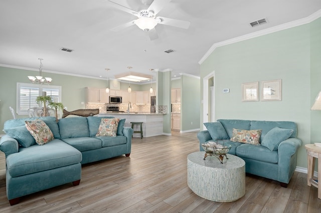 living area featuring ceiling fan with notable chandelier, visible vents, light wood-type flooring, and ornamental molding