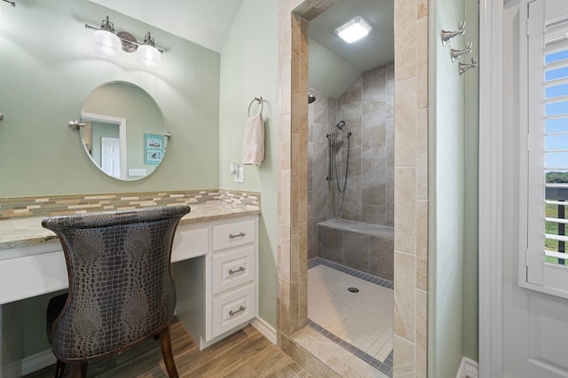 bathroom featuring vanity, hardwood / wood-style flooring, decorative backsplash, and tiled shower