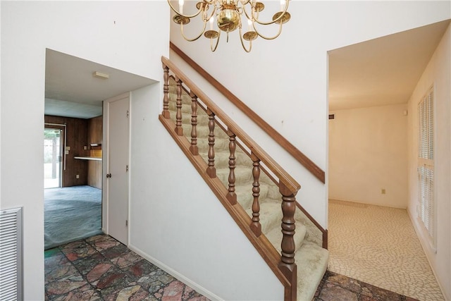 staircase with carpet floors, an inviting chandelier, and wood walls