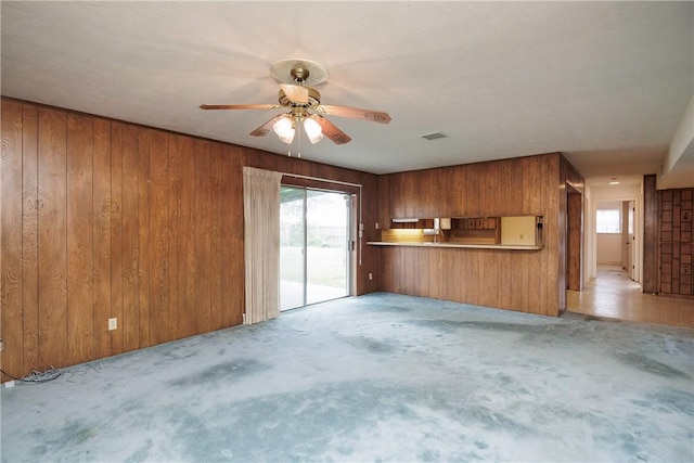 unfurnished living room featuring ceiling fan, light carpet, and wooden walls