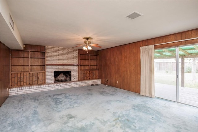 unfurnished living room with carpet flooring, ceiling fan, built in features, a fireplace, and wood walls