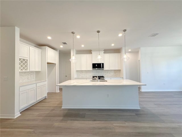 130 Broad Oak Dr, Rockport, TX 78382 - kitchen with stainless steel microwave, backsplash, light wood-type flooring, an island with sink, and recessed lighting