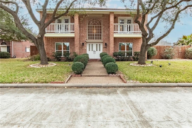 view of front of home with a balcony, a front yard, and french doors