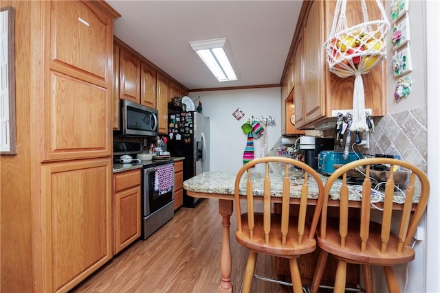10639 Emmord Loop, Corpus Christi, TX 78410 - kitchen featuring appliances with stainless steel finishes, light wood-style flooring, ornamental molding, a kitchen breakfast bar, and light stone countertops