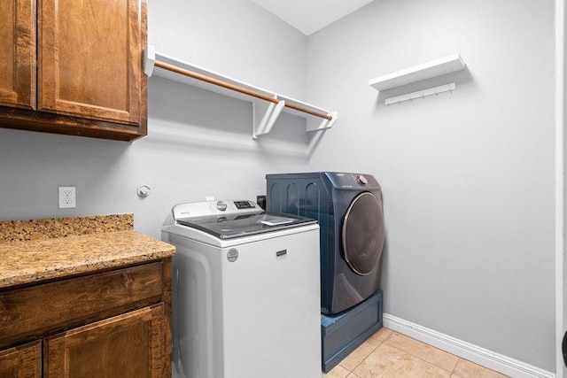 washroom with light tile patterned floors, baseboards, cabinet space, and washing machine and clothes dryer