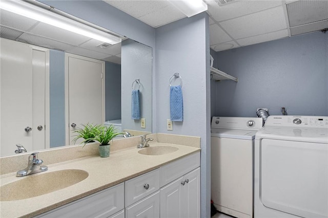 bathroom with a drop ceiling, a sink, washing machine and clothes dryer, and double vanity