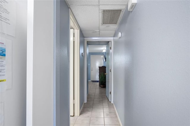 hallway featuring a paneled ceiling, visible vents, baseboards, and light tile patterned floors