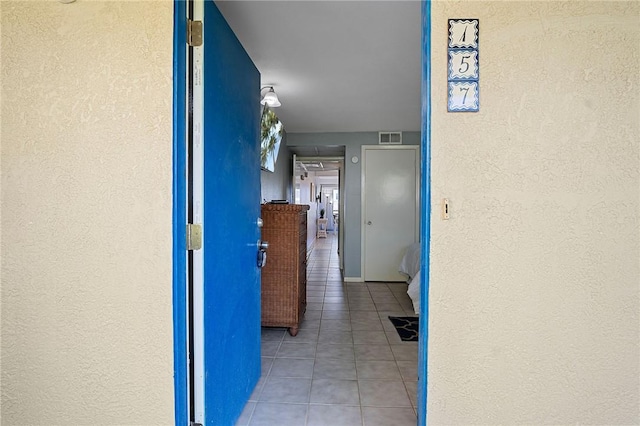 corridor featuring a textured wall, visible vents, and tile patterned floors