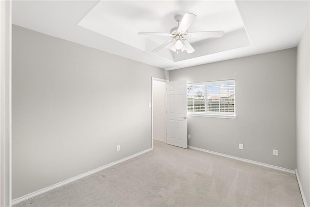 carpeted spare room with a tray ceiling and ceiling fan