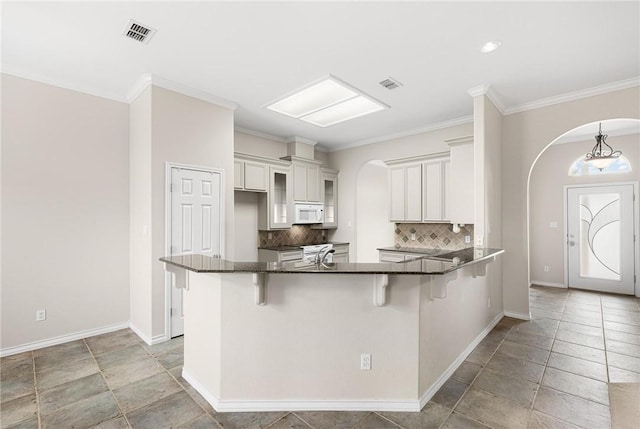 kitchen with kitchen peninsula, crown molding, a kitchen breakfast bar, decorative backsplash, and pendant lighting