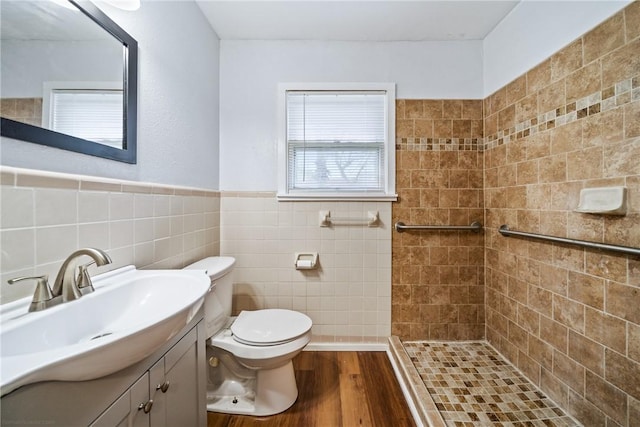 bathroom featuring tiled shower, tile walls, toilet, wood finished floors, and vanity