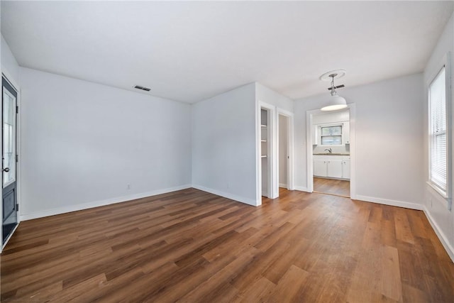 spare room featuring a sink, baseboards, wood finished floors, and plenty of natural light