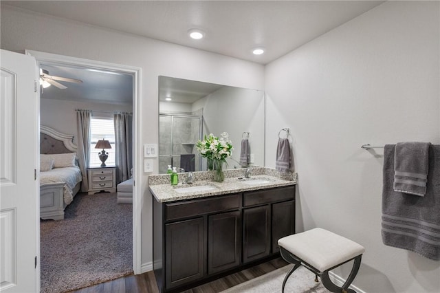 ensuite bathroom featuring connected bathroom, wood finished floors, a sink, a shower stall, and double vanity