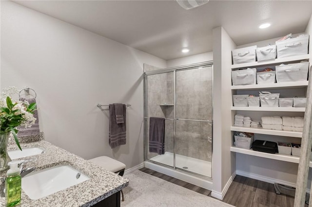 bathroom featuring double vanity, wood finished floors, a stall shower, and a sink