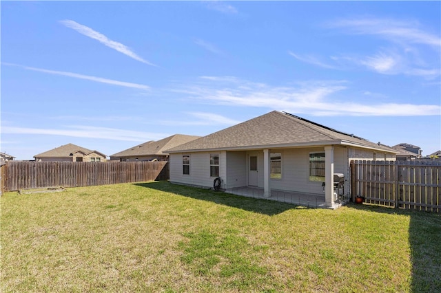 rear view of house with a shingled roof, a fenced backyard, a lawn, and a patio