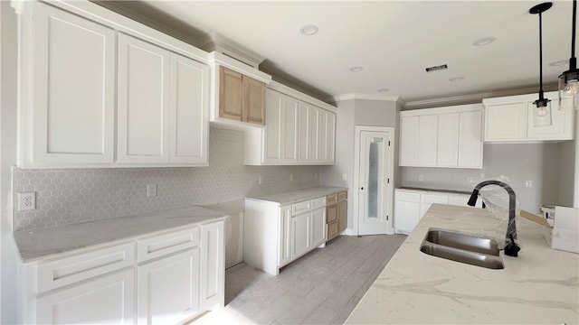 kitchen featuring crown molding, light stone countertops, light wood-type flooring, and a sink