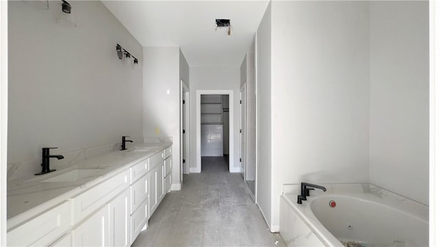 bathroom with double vanity, a walk in closet, a garden tub, and a sink