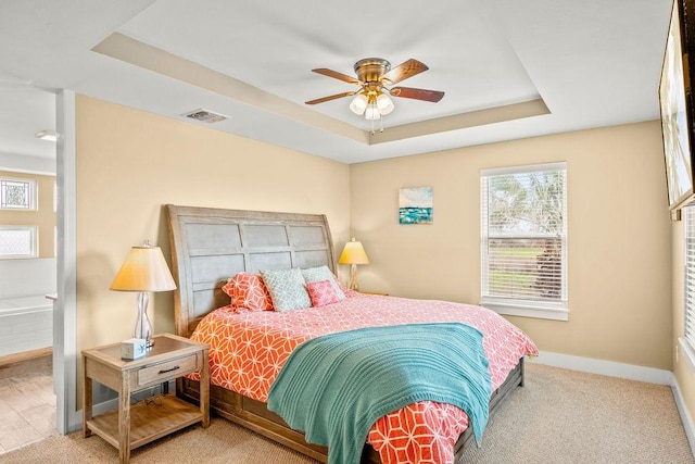 carpeted bedroom featuring a tray ceiling, baseboards, and ceiling fan
