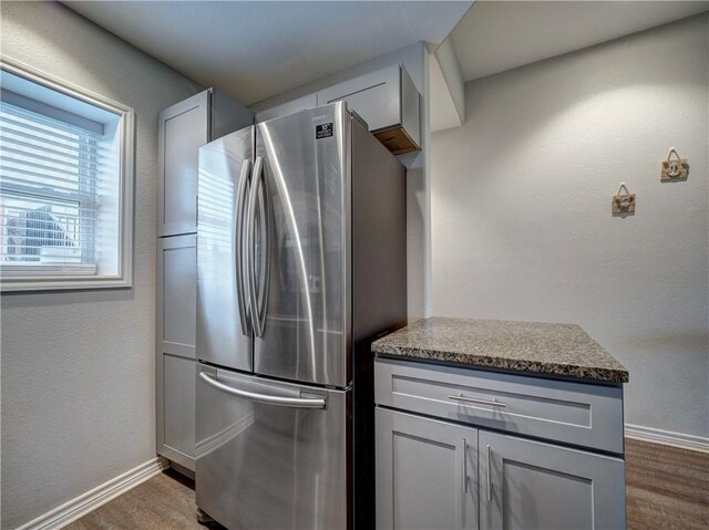 kitchen with gray cabinetry, stainless steel fridge, dark wood-type flooring, and dark stone counters