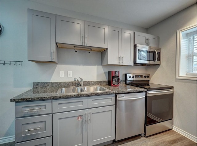 kitchen featuring gray cabinetry, sink, dark stone counters, and appliances with stainless steel finishes