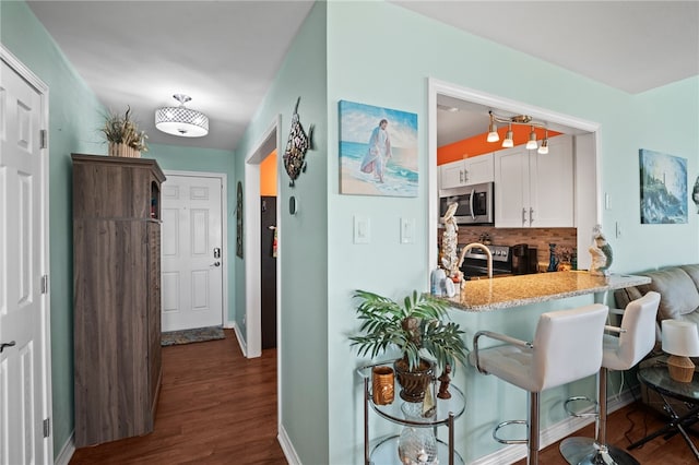 kitchen with stainless steel appliances, backsplash, dark hardwood / wood-style flooring, white cabinets, and a breakfast bar