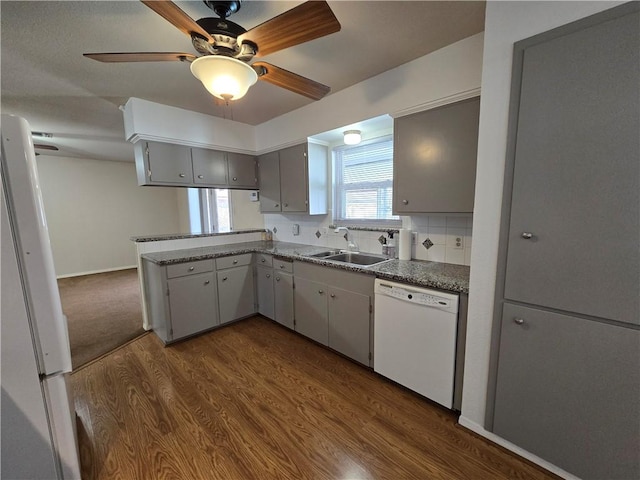 kitchen with white appliances, dark wood-type flooring, a peninsula, a sink, and backsplash