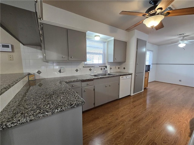 kitchen with a sink, dark wood-style floors, gray cabinets, backsplash, and dishwasher