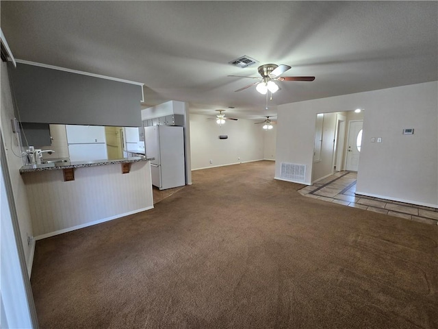 unfurnished living room featuring carpet floors, tile patterned flooring, visible vents, and ceiling fan