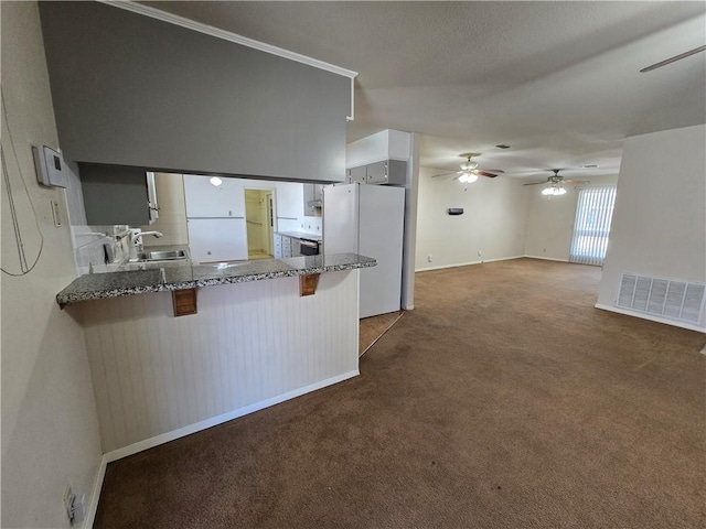 kitchen featuring visible vents, a kitchen breakfast bar, freestanding refrigerator, carpet floors, and a sink