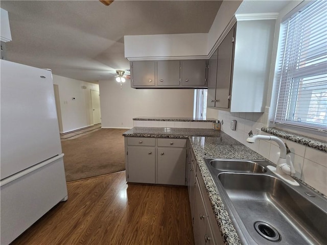 kitchen featuring a peninsula, dark wood-style flooring, a sink, gray cabinets, and freestanding refrigerator