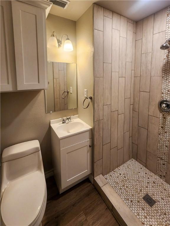 1021 Dona Dr, Corpus Christi, TX 78407 - bathroom featuring a tile shower, vanity, wood finished floors, and toilet