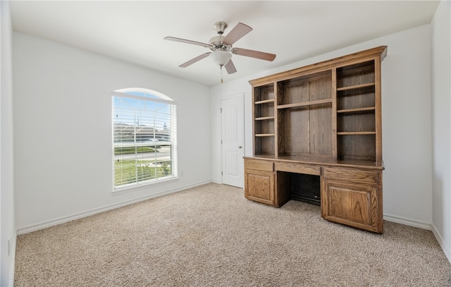 unfurnished office featuring a ceiling fan, light colored carpet, and baseboards