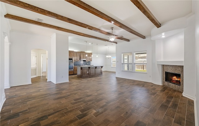 unfurnished living room featuring baseboards, dark wood-type flooring, a lit fireplace, and ceiling fan with notable chandelier