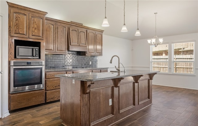 kitchen with decorative backsplash, stainless steel oven, a kitchen breakfast bar, and an island with sink