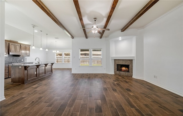 unfurnished living room with dark wood finished floors, ceiling fan with notable chandelier, a warm lit fireplace, and baseboards