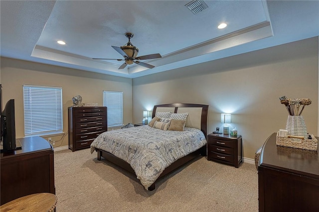 bedroom with visible vents, light colored carpet, and a tray ceiling