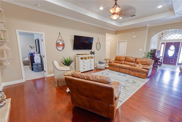 living area with visible vents, ornamental molding, a tray ceiling, and wood-type flooring