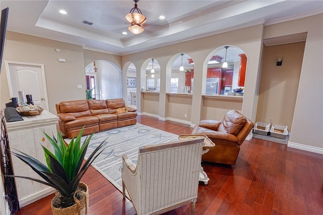 living room with arched walkways, baseboards, a tray ceiling, and wood-type flooring