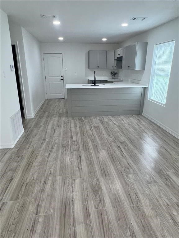 kitchen with gray cabinets, sink, light wood-type flooring, and kitchen peninsula