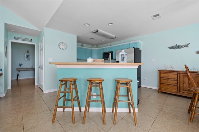 kitchen featuring visible vents, blue cabinets, stainless steel appliances, light countertops, and a kitchen bar