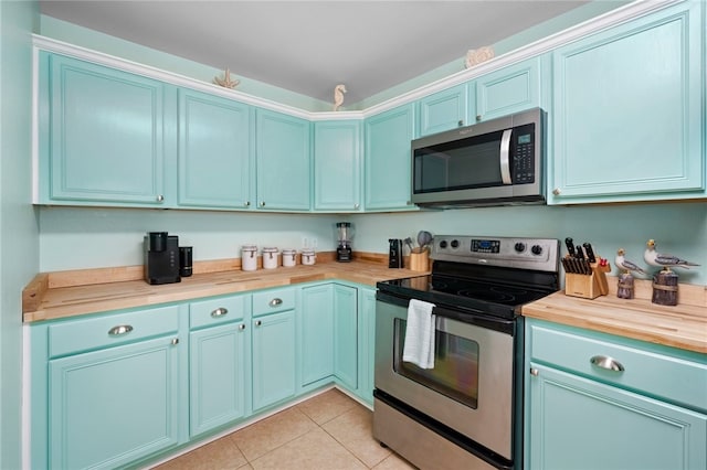 kitchen featuring appliances with stainless steel finishes, wooden counters, and light tile patterned flooring